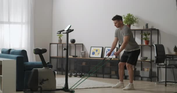 사람은 스 포티 고무 밴드 로 이두근과 삼두근을 훈련시키고 있으며, 가정용 현대 스 포오 츠 장비를 갖춘 아파트 에서 운동을 하고 있다 — 비디오