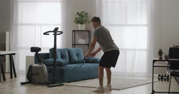 Thuisfitness van de jongeman, lichaamsbeweging thuis, training met elastiekje, gespannen armspieren — Stockvideo