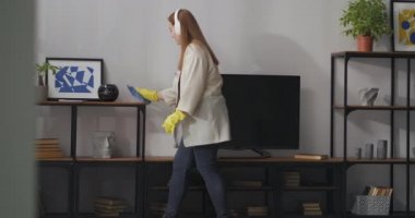 Dairenin tozunu ve temizliğini genç ev hanımı mendil, temizlik ve temizlik hizmetleriyle rafları siliyor.