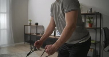 Sportif genç adam evde antrenman yapıyor. Kauçuk bantları kollarıyla geriyor. Vücut şekli için kaslarını geriyor.