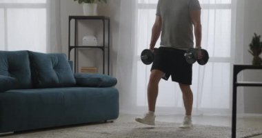 Yetişkin ve güçlü bir adam ağırlık egzersizleri yapıyor, ellerinde dambıllarla çömeliyor, spor salonunda güç antrenmanı yapıyor.