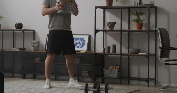 Homme athlétique est accroupi avec des livres dans les mains dans la chambre, entraînement de force pour garder la forme, remise en forme à la maison — Video