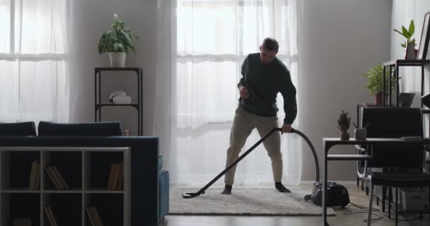 Rolig kille dansar med dammsugare i lägenhet, städa hemma och ha kul i modern inredning — Stockvideo