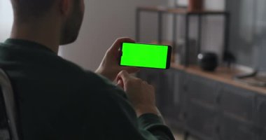Erkek kullanıcı modern akıllı telefonun dokunmatik ekranına dokunuyor, aygıtı yatay olarak tutuyor, kromakey için yeşil ekran
