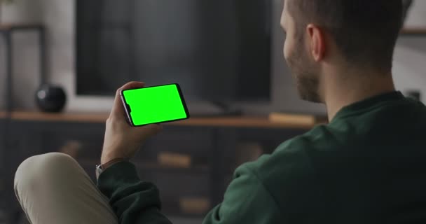 男は家の無線LANでスマートフォンのビデオ会議でチャットしているガジェットのクロマキー技術のための緑の画面 — ストック動画