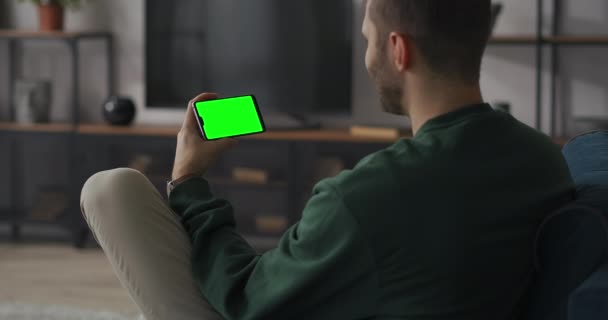 Hombre alegre se está comunicando por videollamada en el teléfono inteligente con chromakey, el usuario está sosteniendo gadget con pantalla verde horizontal — Vídeos de Stock