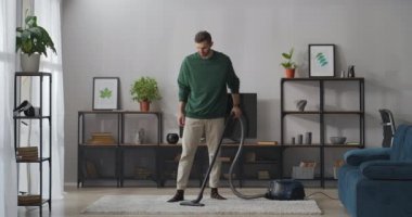 Adam, modern dairenin oturma odasında elektrikli süpürgeyle temizlik yapıyor. Ev işlerine yardım ediyor.