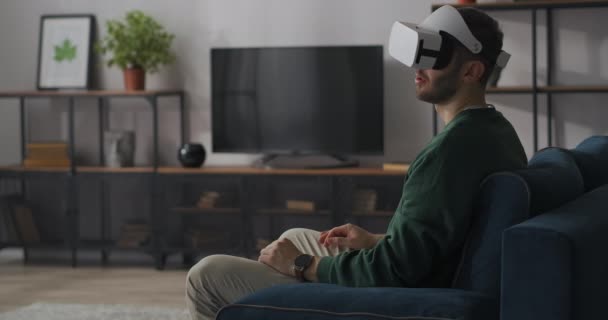 Volwassen man is het bekijken van 3D-video met behulp van head-mounted display en virtual reality-technologie, zittend op de bank thuis, moderne technologie — Stockvideo