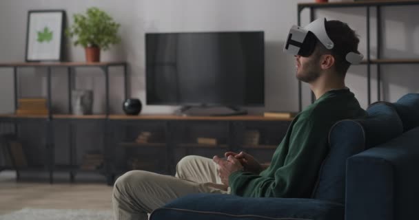 Чоловічий геймер грає онлайн з дисплеєм на голові і джойстиком, сидячи один у вітальні на дивані — стокове відео
