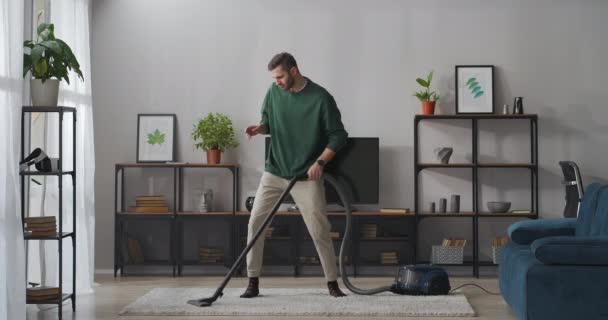 Zabawny dorosły mężczyzna robi czyszczenie dywanu, za pomocą odkurzacza i tańca, zabawy podczas sprzątania domu — Wideo stockowe