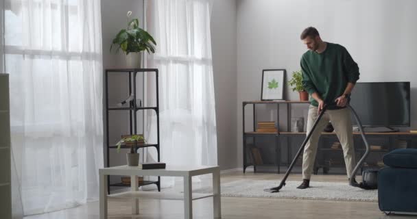 Vuxen stilig man svävar matta i lägenhet, med hjälp av dammsugare för städning rum på helgen — Stockvideo