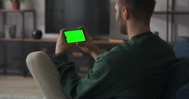 Homme adulte utilise smartphone avec écran vert pour clé chromatique, concept de chat en ligne, tenant gadget horizontalement — Video