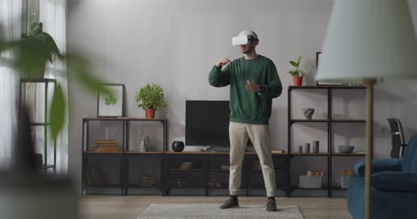 Joven está utilizando la pantalla montada en la cabeza de pie en la sala de estar y deslizando la pantalla virtual por las manos, de larga duración — Vídeo de stock