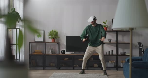 Jeune homme utilise la réalité virtuelle pour se divertir, chanter et danser dans la salle, s'amuser seul à la maison — Video