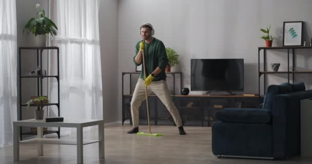 Ensam man har roligt under sanering hemma, tvätta golvet och sjunga i mopp, lyssna på musik med hörlurar — Stockvideo
