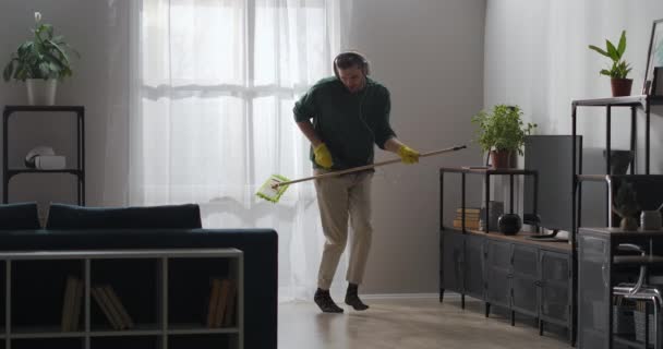 男は家で掃除をしてモップと踊ってリビングで床を洗ってギターのようにモップで遊んでる — ストック動画