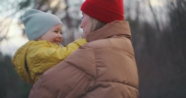 Genç bir anne oğlunu kollarında tutuyor. Dilini çocuğa uzatıyor. Neşeyle gülmeye başlar ve gözlerini kısar. Sonbaharda ormanda çekim yapmak. Ağır çekim. Orta boy..
