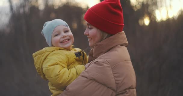 A young mother holds her little son in her arms. Look at him tenderly, and the boy looks at the camera and laughs cheerfully. then turns his head and looks at Mom. Slow motion. Medium shot. — Stock Video