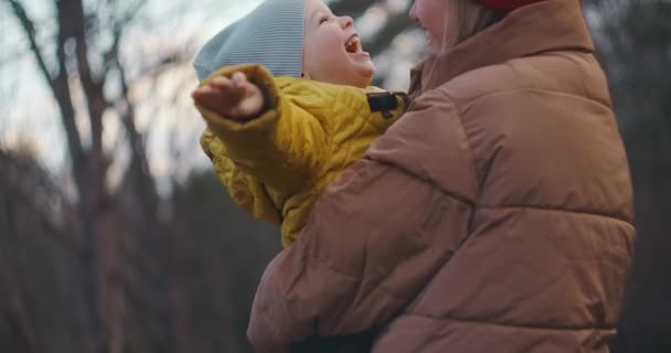 En ung mor tog sin son i famnen. Pojken börjar skratta högt och slår sin mor på kinderna med handflatorna. De är lyckliga tillsammans. Skjuter i skogen på hösten. Långsamma rörelser — Stockvideo