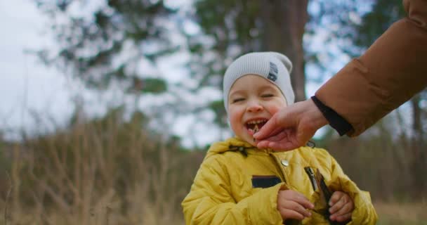 Een jongetje van 2 jaar oud leert de wereld kennen, proeft een houten tak. Mam haalt het vuilnis uit zijn mond. Het kind raakt de tong met een vinger, de moeder slaat hem op de hand. — Stockvideo