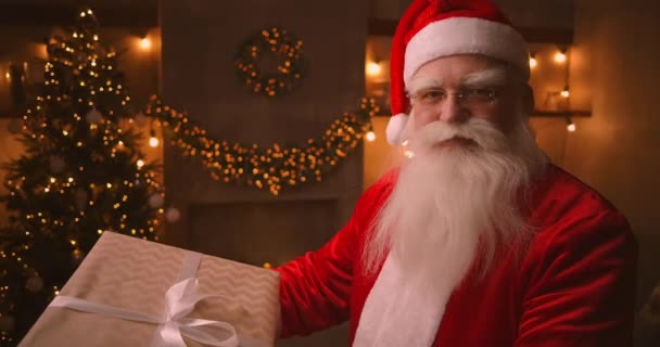 Jultomten håller och skakar en stor vacker låda med en present till ett lydigt barn för en lycklig jul. Titta på kameran och le. Medelhög skott. — Stockvideo