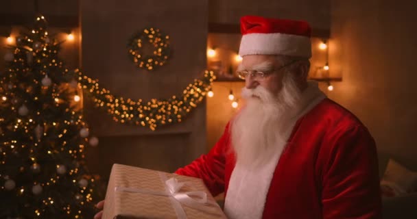 Papai Noel segura em suas mãos uma grande caixa bonita com um presente para uma criança obediente para o Feliz Natal. Olha para a câmara e sorri. — Vídeo de Stock