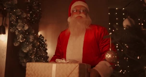 Santa Claus se inclina y pone una hermosa caja grande con un regalo para un buen niño bajo el árbol de Navidad para el niño. — Vídeos de Stock