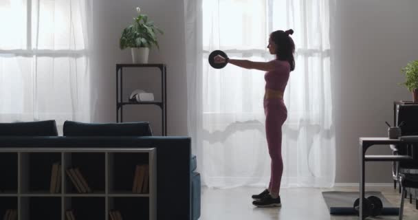 Mujer joven vestido traje rosa está haciendo sentadillas con peso en el apartamento, entrenamiento en casa, los músculos de trabajo del cuerpo, delgada — Vídeo de stock