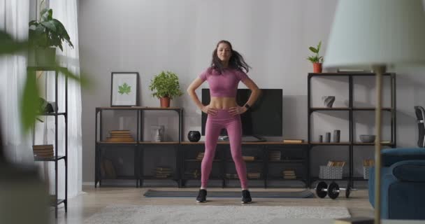 Ung kvinna gör aerobics övningar hemma, klädda sportkläder för hemmaträning, hoppa i vardagsrummet, hälsosam livsstil — Stockvideo