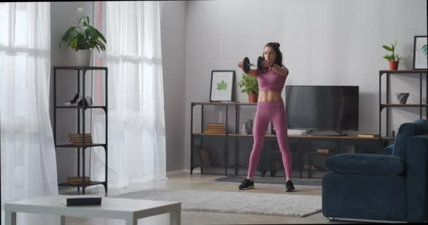 Kobieta przysiada z ciężarem w rękach, trening w salonie nowoczesnego mieszkania, fitness domu młodej sportowej pani — Wideo stockowe