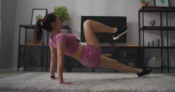 Спортивная активность дома при самоизоляции, стройная женщина тренирует свое тело в квартире, упражнения для мышц ног — стоковое видео