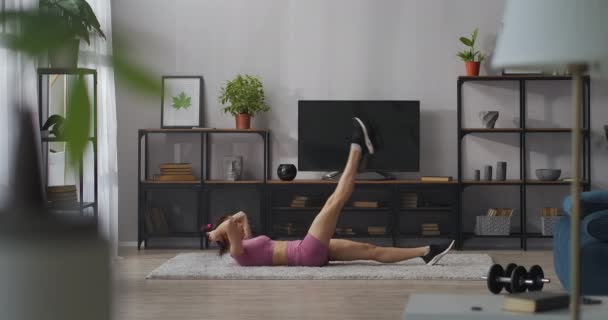 Güçlü bir kadın, evde çalışırken, yerde yatarken, oturma odasında çalışırken, karın ve bacaklar için egzersiz yapıyor. — Stok video