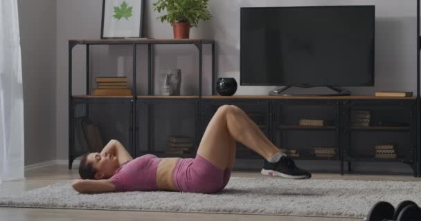 Entrenamiento de los músculos abdominales en casa, joven mujer deportiva está haciendo giros del torso en la sala de estar, acostado en la alfombra, actividad deportiva — Vídeo de stock