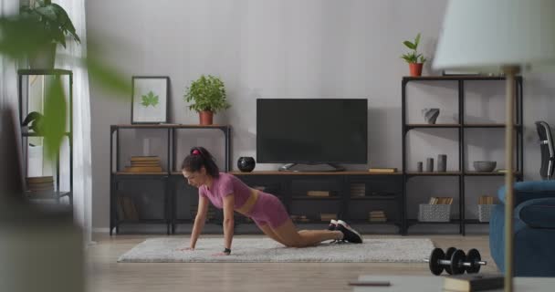 Mujer joven está haciendo flexiones en el apartamento, entrenamiento en casa para mantenerse en forma y culturismo, señora deportiva y atlética — Vídeo de stock