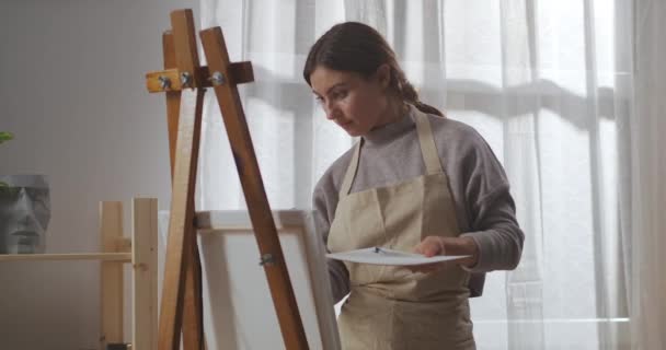 Geïnspireerde vrouwelijke schilder werkt in atelier, op doek getekend door penseel, kunstwerk, schilderkunst — Stockvideo