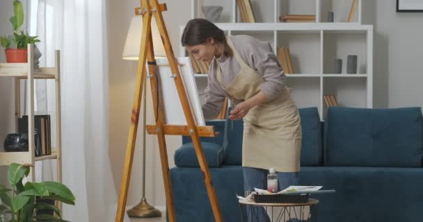 Σχέδιο γυναίκα σε άνετο διαμέρισμα, χρησιμοποιώντας επαγγελματικό καβαλέτο, καμβά, χρώμα και πινέλο, ταλαντούχος νεαρός καλλιτέχνης — Αρχείο Βίντεο