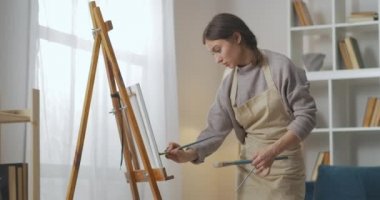 Kendini izole etme sırasında evde hobi, kadın sanatçı oturma odasında tuvale resim çiziyor, orta boy portre.