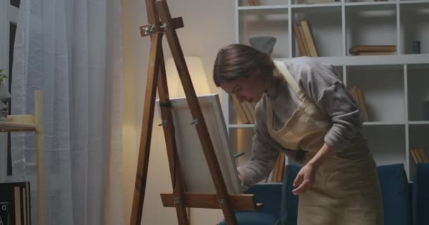 Middelmatig portret van tekenvrouw 's avonds thuis, met professionele ezel, doek, verf en penseel, getalenteerde jonge kunstenaar — Stockvideo