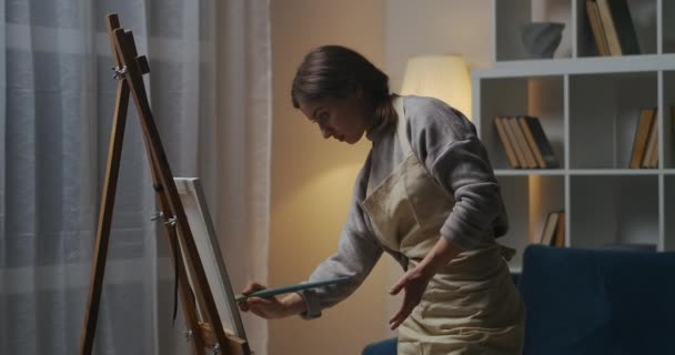 Γυναίκα καλλιτέχνης ζωγραφίζει σε καμβά στο σπίτι το βράδυ, ζωγραφίζοντας εικόνα στο διαμέρισμα, κάνοντας χόμπι στο σπίτι το Σαββατοκύριακο — Αρχείο Βίντεο