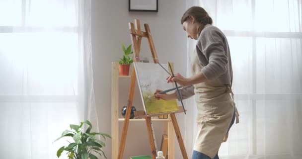 Mujer artista está dibujando paisaje sobre lienzo en la sala de estar, pasar tiempo en el fin de semana en casa, hobby creativo — Vídeos de Stock