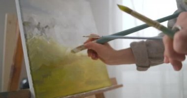 Ressam, kadın ressamın çalışmaları sırasında tuvaldeki resme yakından bakmak için profesyonel boya fırçasını bez üzerine renk uygulamak için kullanıyor