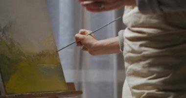 Ressam kadın tuvale manzara çiziyor, akşamları apartmanda hobi yapıyor, resme ve kadın ressamın yüzüne yakın çekim yapıyor.