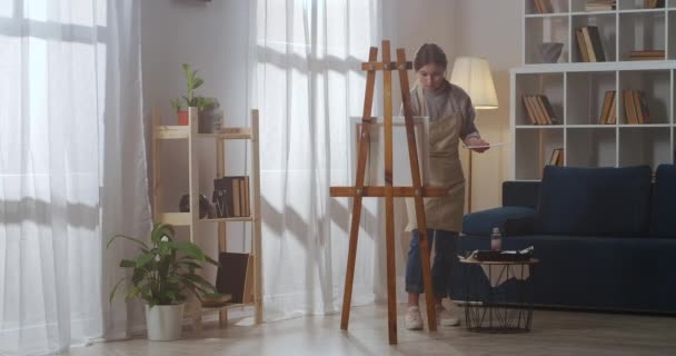 Σπίτι εργασίας στούντιο της νεαρής γυναίκας ζωγράφος, καλλιτέχνης εργάζεται με πινέλο και βαφές, σχέδιο εικόνα σε καμβά — Αρχείο Βίντεο