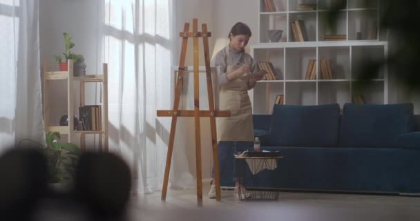 Σπίτι εργασίας στούντιο της νεαρής γυναίκας ζωγράφος, γυναίκα αναμιγνύει τα χρώματα και σχέδιο σε καμβά στο διαμέρισμα — Αρχείο Βίντεο