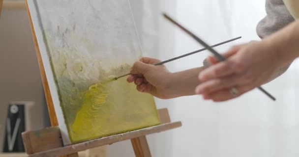 Detail zicht op doek met landschap in artistieke studio, vrouwelijke kunstenaar is tekenen door penseel en olieverf — Stockvideo