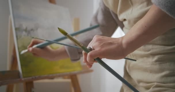 Artista paisagista está trabalhando em estúdio, pintura quadro por pincel e corantes de óleo, close-up vista sobre tela com imagem — Vídeo de Stock