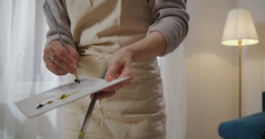 Genç bir kadının sanat eseri ve hobisi, ressam tuvale resim çiziyor, paletin renklerini karıştırıyor ve resme uyguluyor.