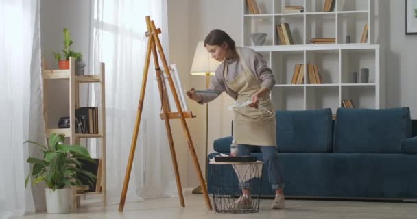 Full-length shot van kunstenaar vrouw thuis kunst studio, schilderen met olieverf en borstel op doek, staan in de buurt van ezel — Stockvideo