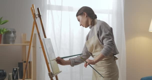 Giovane bella donna sta trascorrendo del tempo nel fine settimana con calma, facendo hobby creativo, disegno su tela, ritratto medio — Video Stock