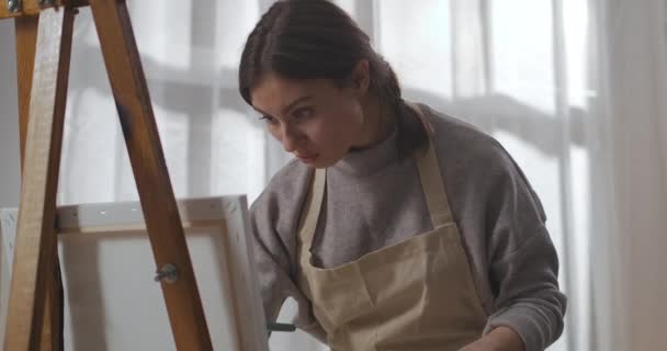 koncentrovaná žena kreslí obraz barvami na plátno v pokoji, umělec pracuje v domácím studiu